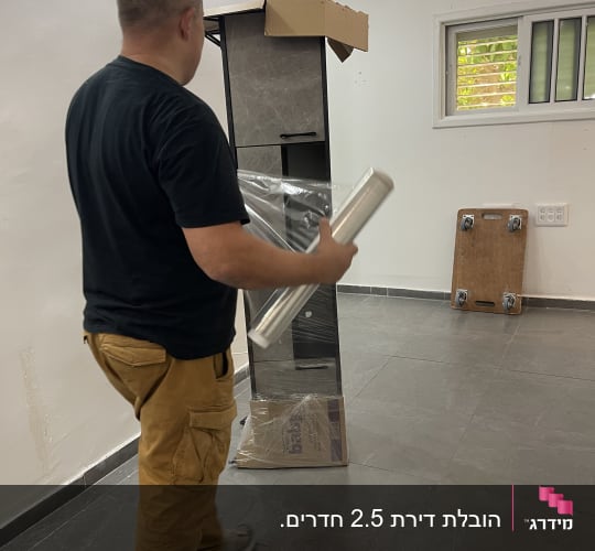 אדם מחזיק גליל ניילון ליד ארון קרטון